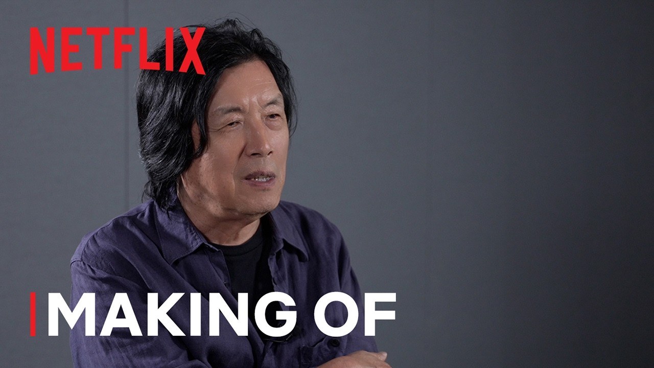 Lee Chang-dong, de camisa azul-escura, falando numa entrevista de bastidores de Amor Possível, com o logo da Netflix e a legenda Making Of