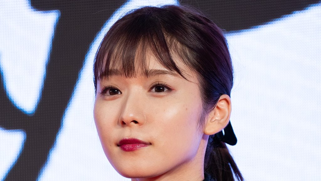 Mayu Matsuoka de franja, batom vermelho e laço preto no cabelo, olhando para o lado