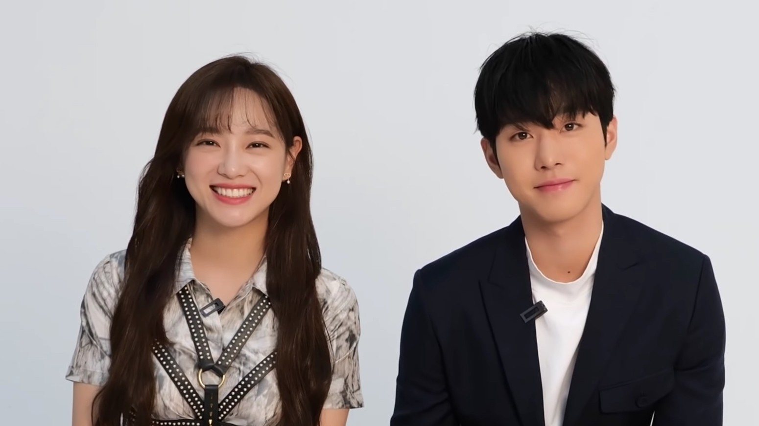 Kim Se Jeong, de vestido estampado, e Ahn Hyo Seop, de terno escuro, sentados lado a lado diante de fundo claro, em entrevista de divulgação de Business Proposal