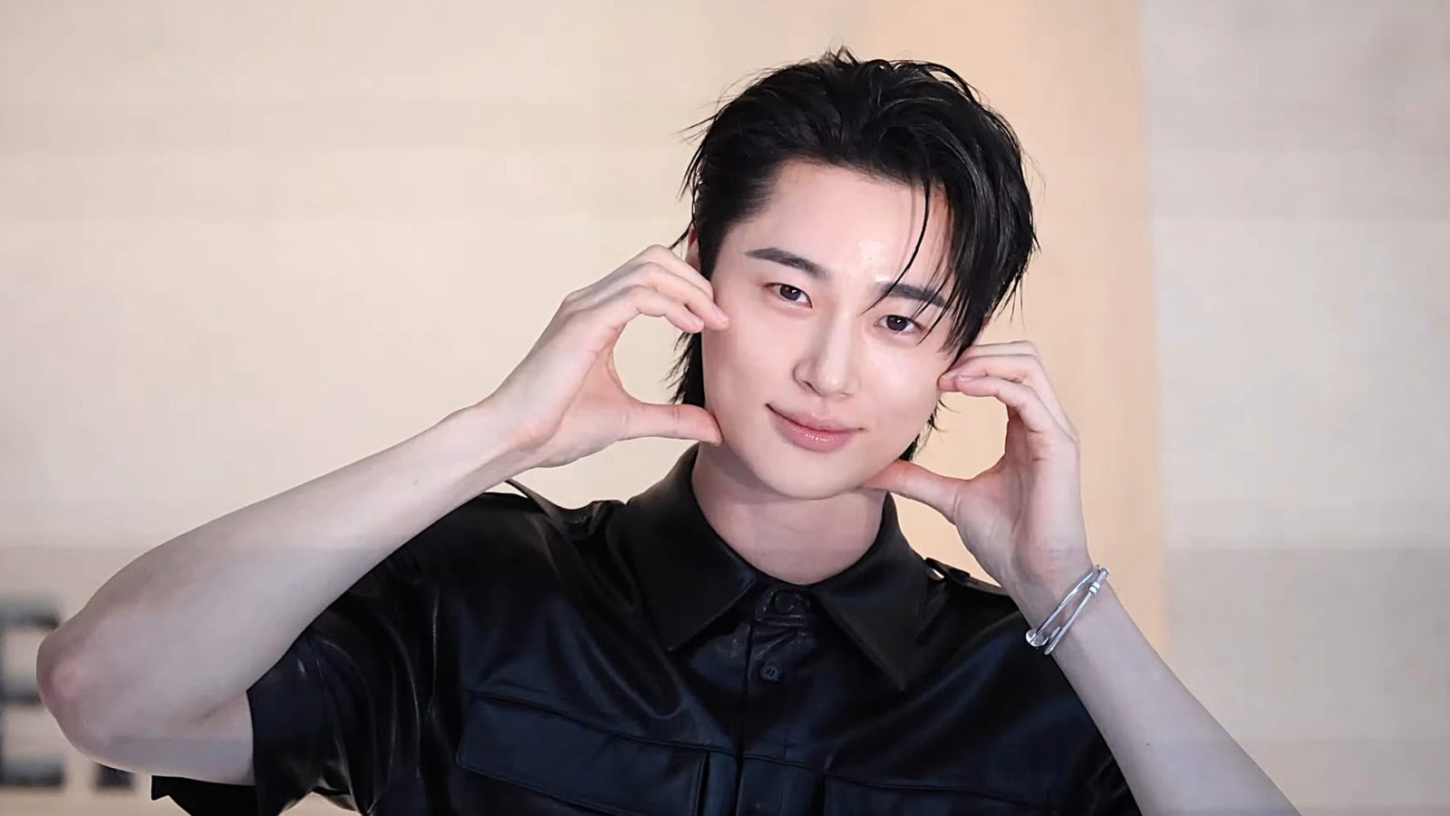 Byeon Woo-seok de camisa preta sorri e emoldura o rosto com as duas mãos
