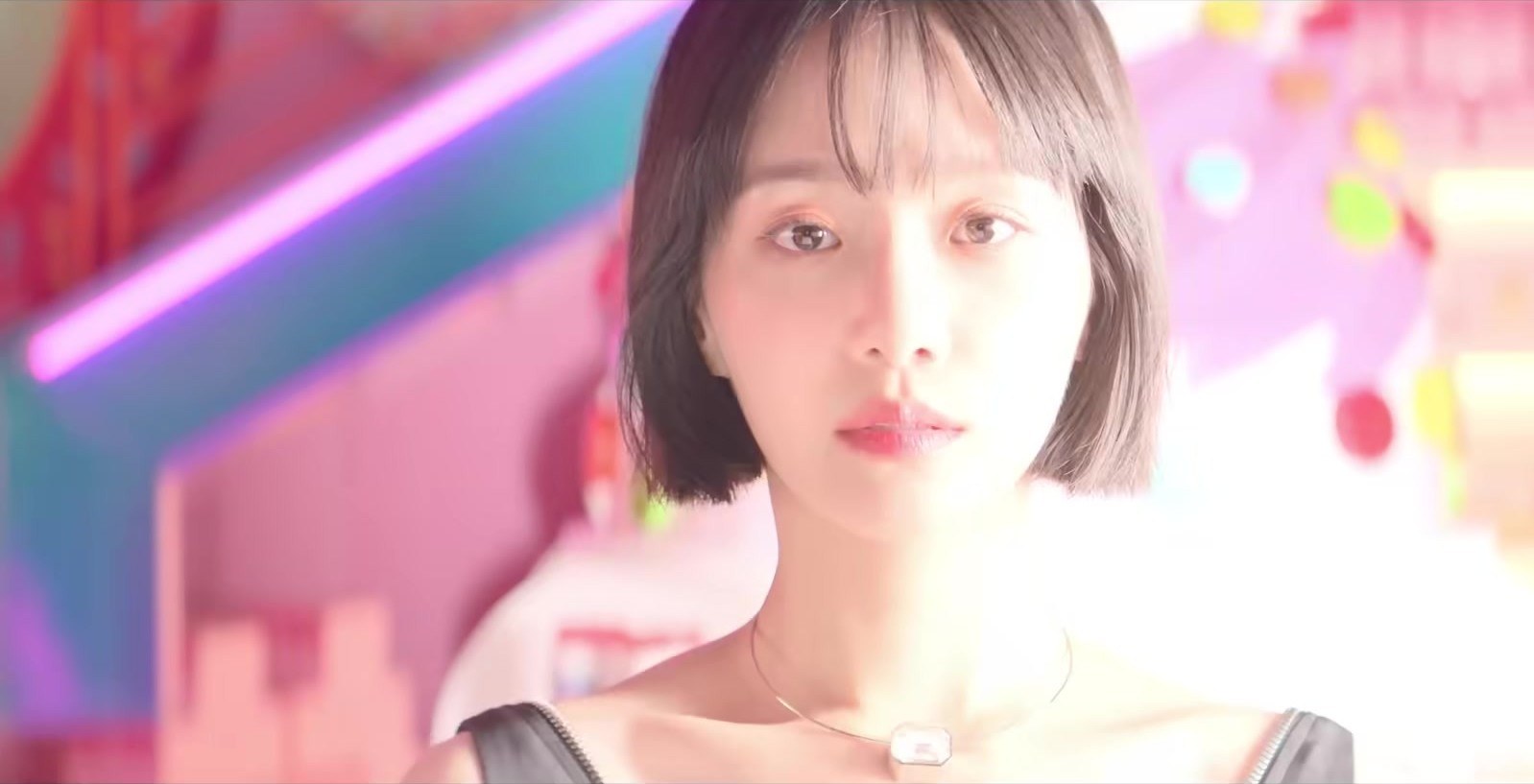 Jovem de franja curta e colar, em quadro do trailer oficial de Celebrity, com neon rosa e roxo ao fundo