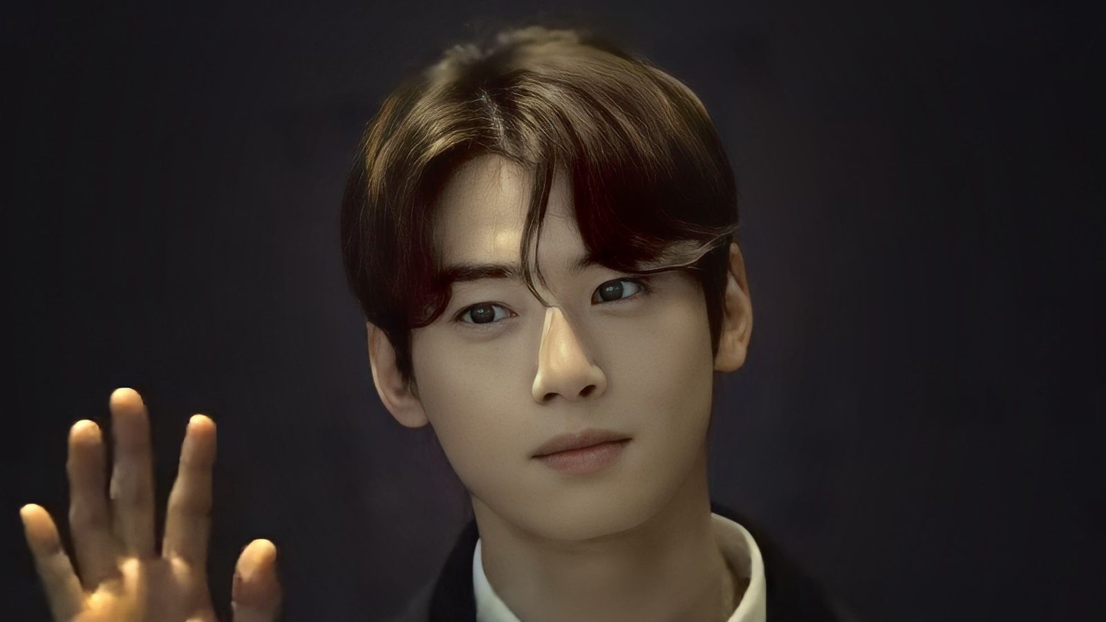 Cha Eun-woo de casaco escuro e camisa clara acenando com a mão aberta diante de fundo escuro