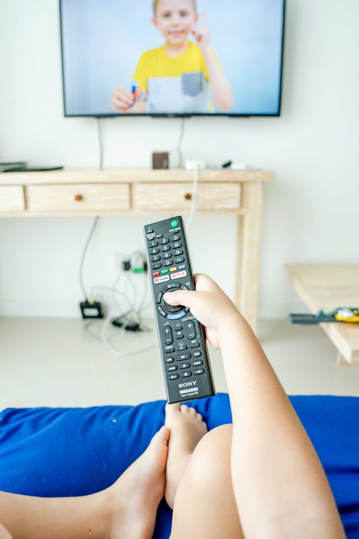 Mão aponta um controle remoto para uma televisão