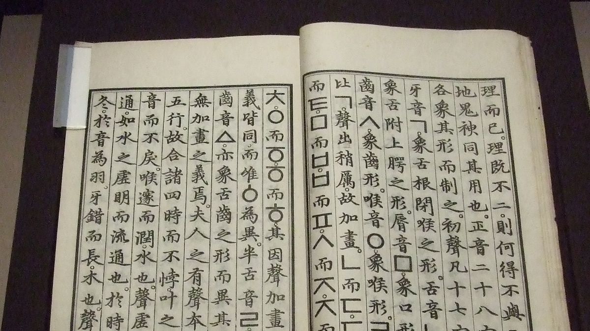 Livro aberto em vitrine com colunas de caracteres chineses e letras do alfabeto coreano, entre elas o círculo ㅇ e a letra ㄱ