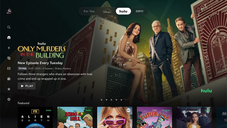 Tela inicial de streaming com as abas For You, Disney+, hulu e ESPN no alto, a aba hulu selecionada e o destaque de Only Murders in the Building com três atores diante de cartas gigantes