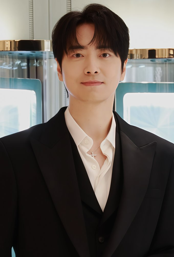 Lee Jun-hyuk, de terno preto e camisa branca aberta no colarinho, sorri em evento de marca