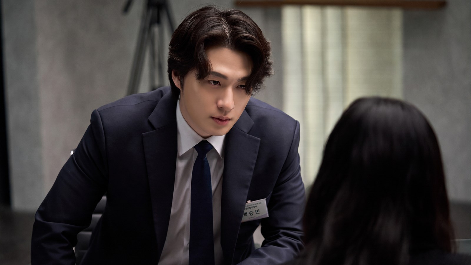 Shin Seung Ho de terno e crachá, inclinado sobre uma candidata de costas, em cena de Final Interview