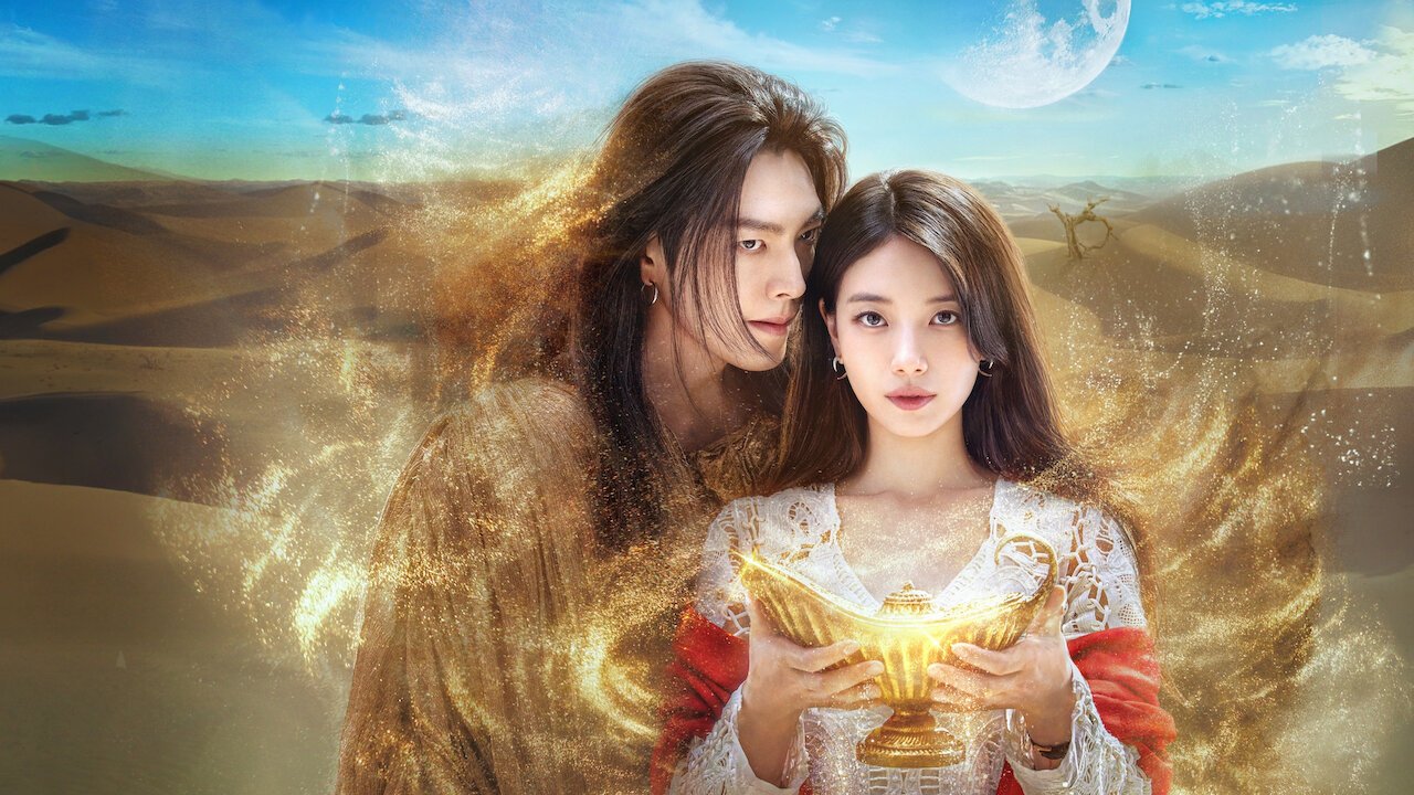 Kim Woo-bin, de cabelos longos e manto marrom, atrás de Suzy, que segura uma lâmpada dourada, num deserto com redemoinho de areia brilhante e lua no céu