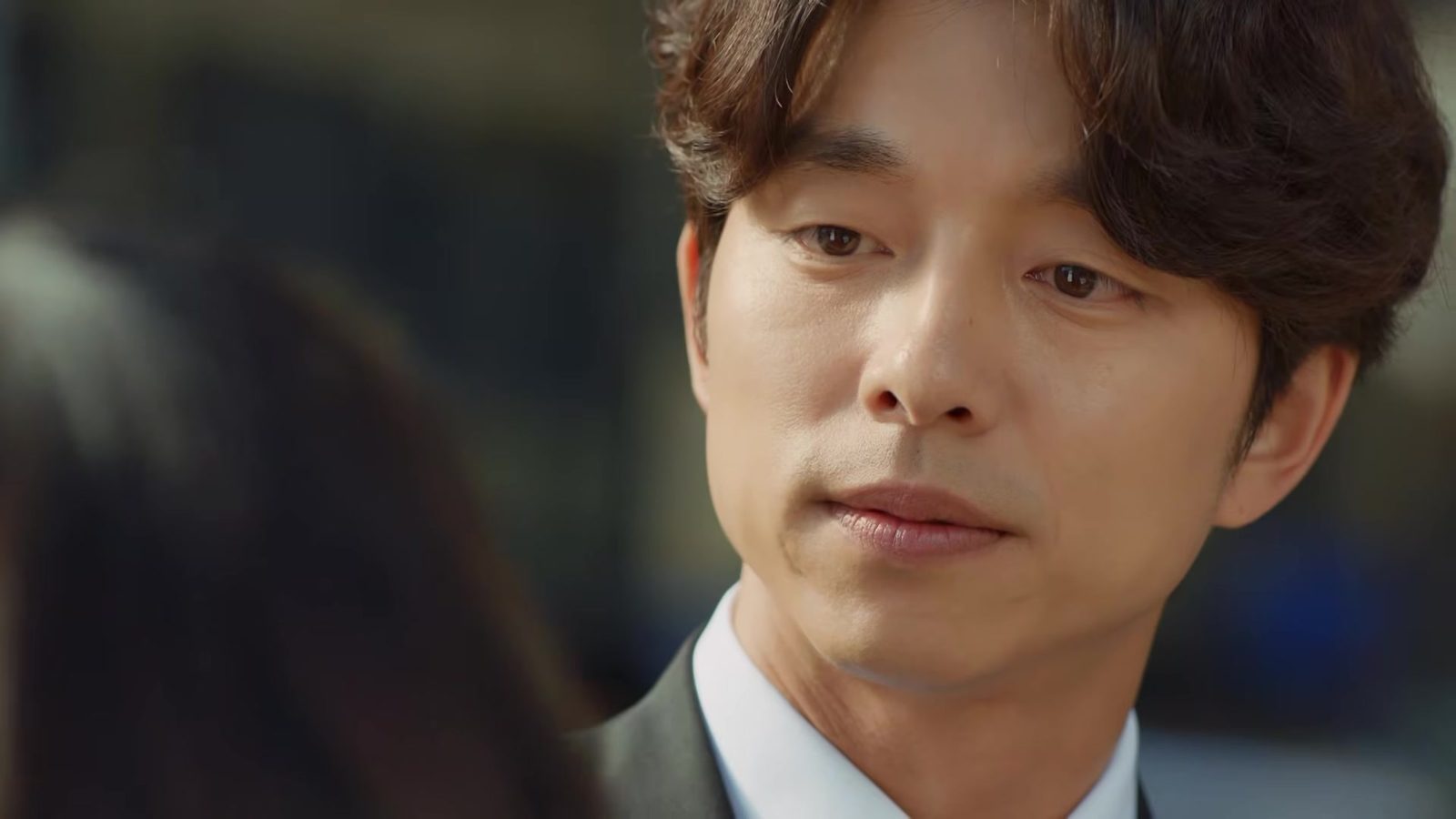 Gong Yoo de terno cinza e camisa branca, em close, em quadro do trailer oficial de Goblin