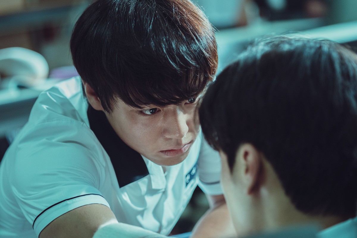 Park Ji-hoon como Si-eun, de uniforme escolar branco, encara de muito perto um colega de costas
