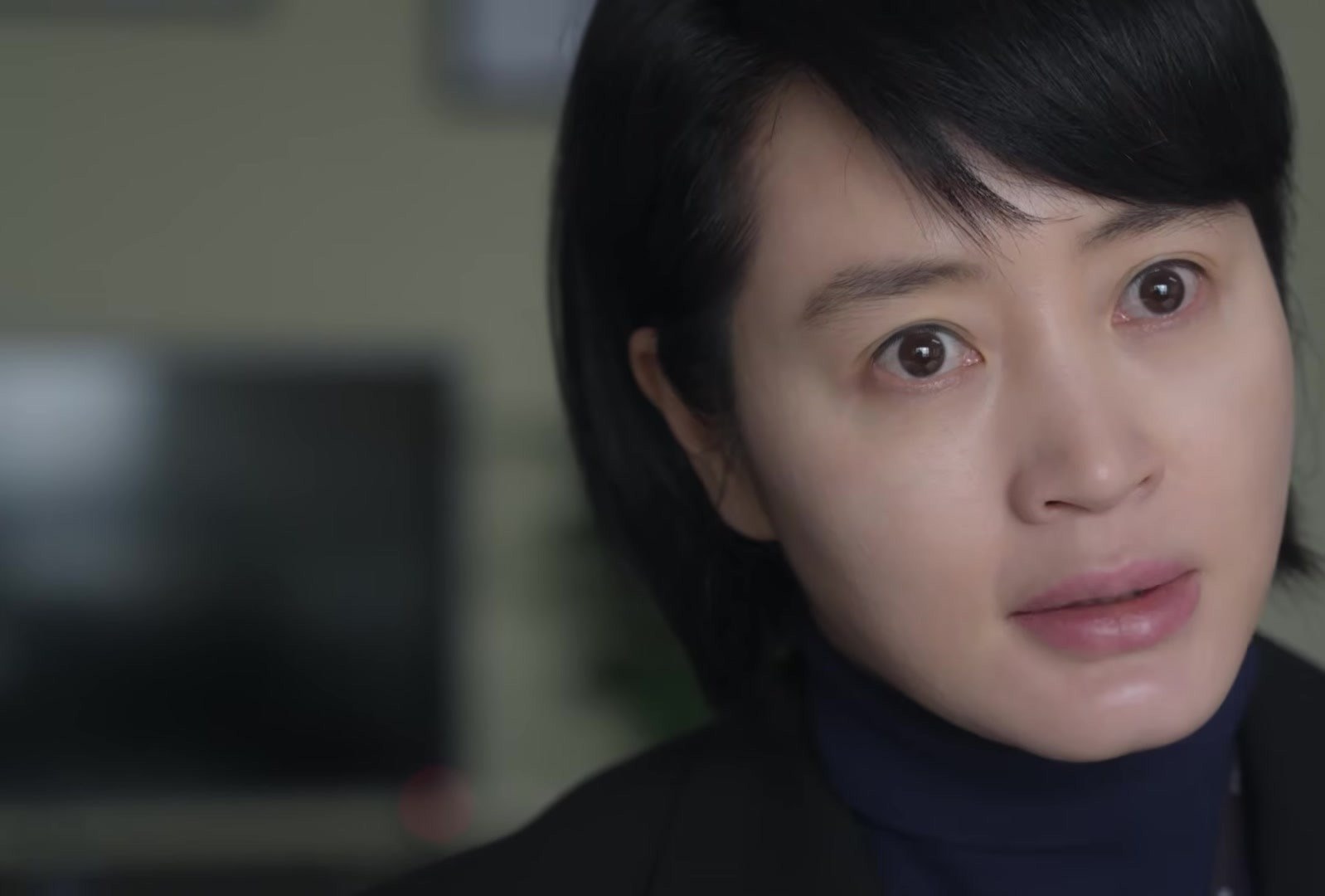 Close de Kim Hye-soo, de cabelo curto e gola azul-marinho, olhando com os olhos arregalados, em cena do trailer de Juvenile Justice