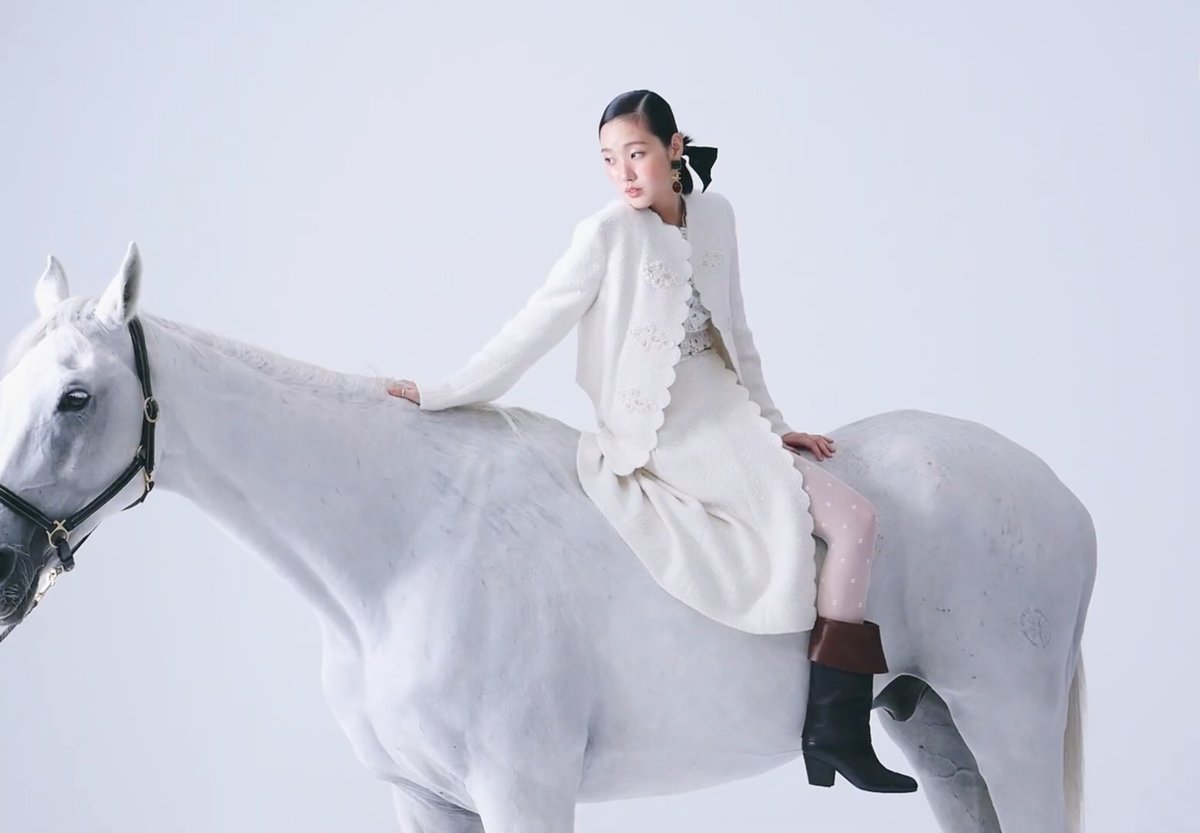Kim Go-eun de conjunto branco sentada sobre um cavalo branco em estúdio de fundo claro
