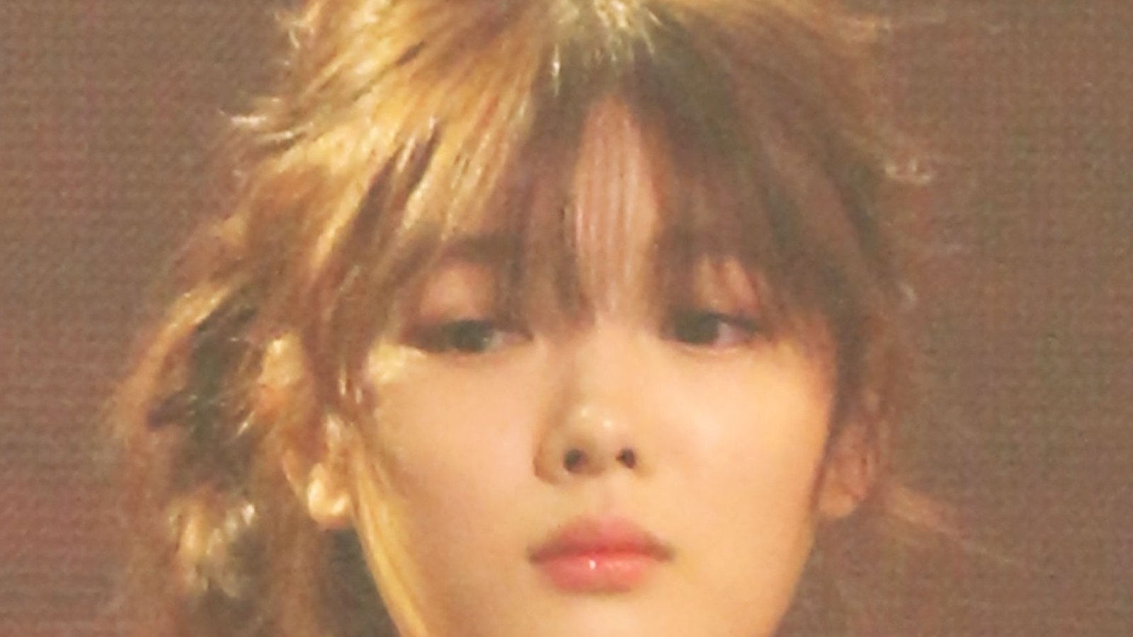 Kim Yoo-jung de franja e cabelo preso, com vestido preto de um ombro só, diante de fundo avermelhado