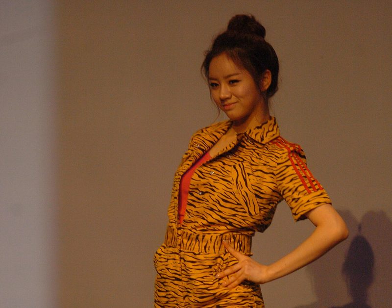 Lee Hye-ri de coque, conjunto de estampa de tigre, sorrindo com a mão na cintura num palco
