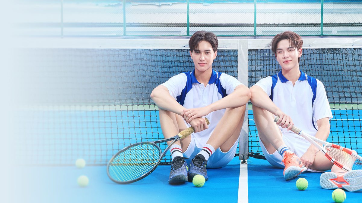 Dois rapazes de camisa polo branca e short, sentados no chão de uma quadra de tênis azul encostados na rede, cada um com uma raquete, com bolas de tênis espalhadas ao redor
