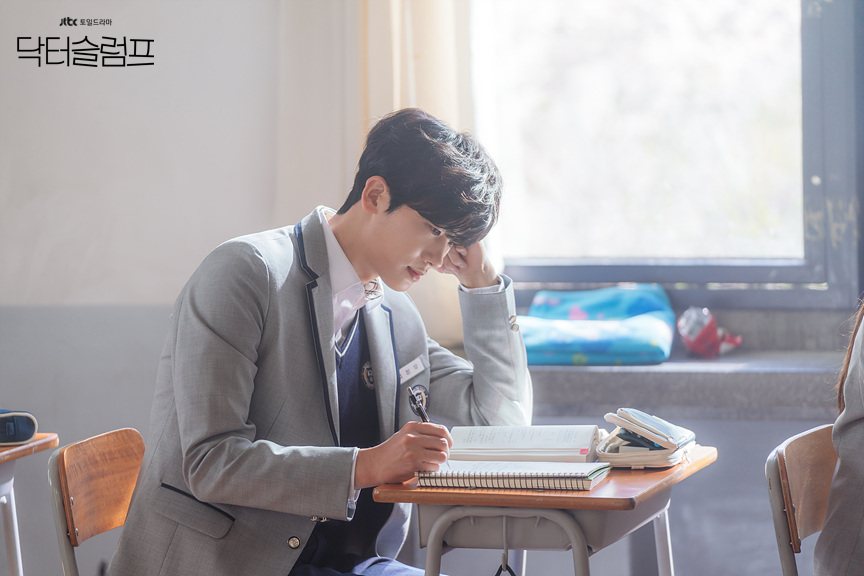 Park Hyung-sik como o estudante Yeo Jeong-woo, de uniforme escolar cinza, escrevendo num caderno em uma carteira junto à janela da sala de aula