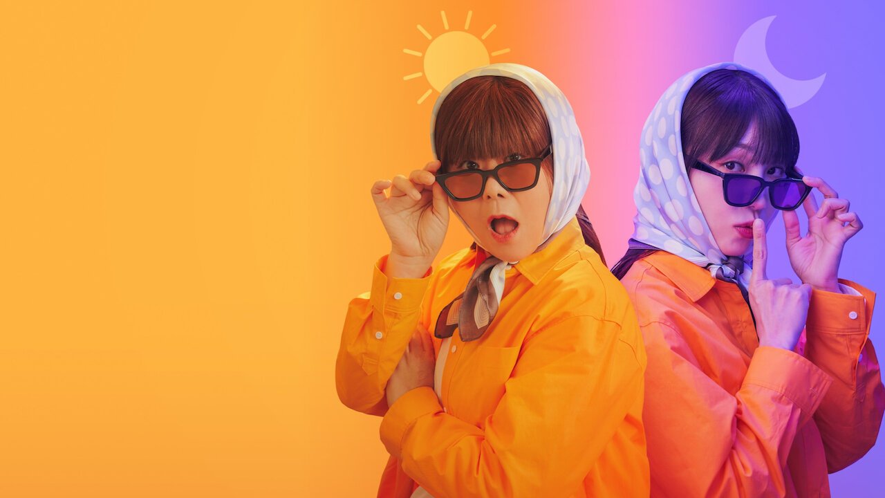 Lee Jung-eun e Jeong Eun-ji com a mesma capa laranja, lenço na cabeça e óculos escuros, lado a lado sob os desenhos de um sol e de uma lua