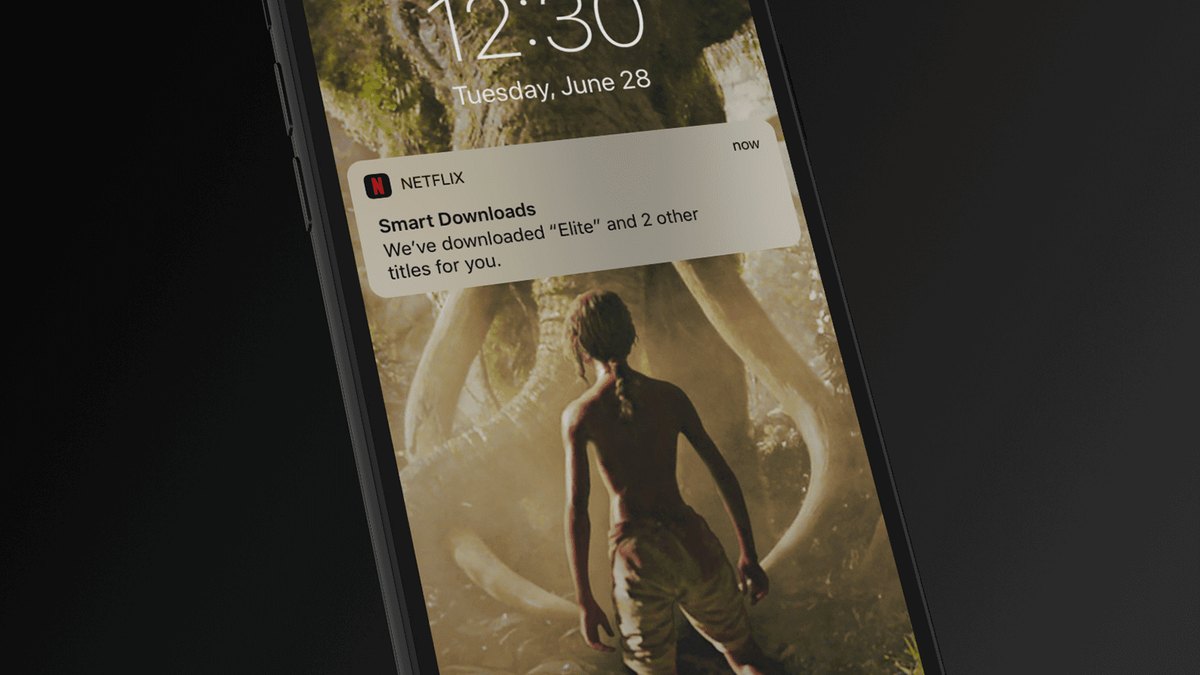 Celular inclinado com a tela de bloqueio mostrando uma notificação da Netflix sobre downloads automáticos, sobre fundo escuro