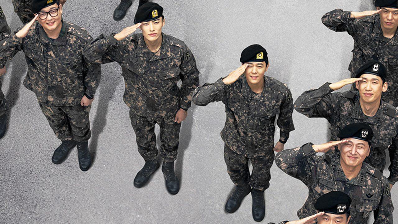 Soldados de boina preta e uniforme camuflado batem continência olhando para cima, vistos do alto sobre um fundo cinza