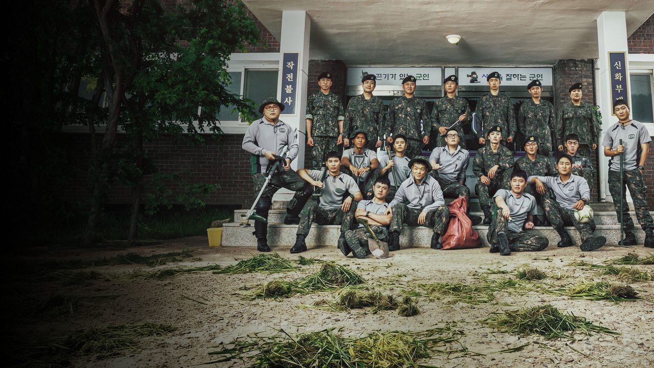 Cerca de vinte soldados de uniforme camuflado e camiseta cinza posam nos degraus de um prédio de quartel, com capim cortado no chão