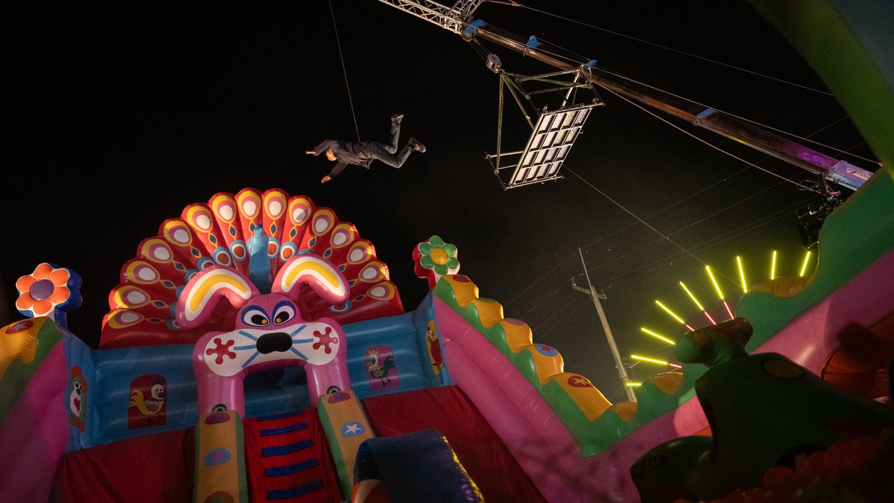Escorregador inflável colorido iluminado à noite, com um dublê pendurado por cabos e equipamento de filmagem no alto