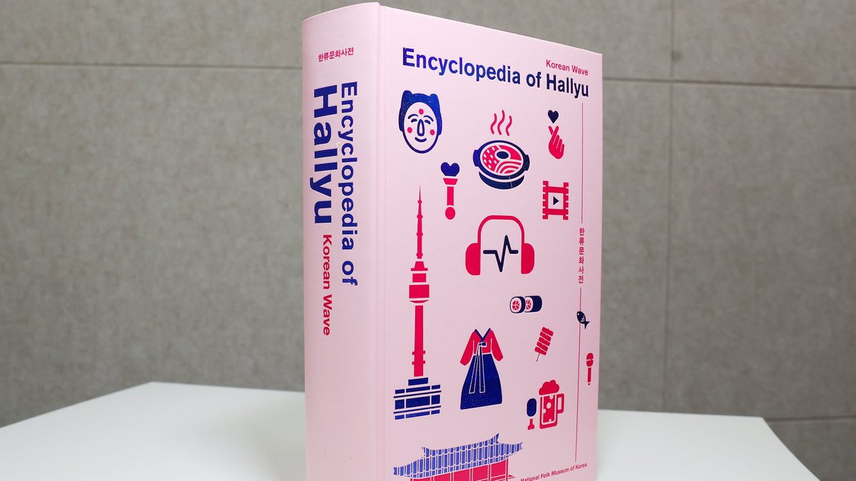 A Encyclopedia of Hallyu em pé, vista de lado, com a lombada rosa e o título em azul