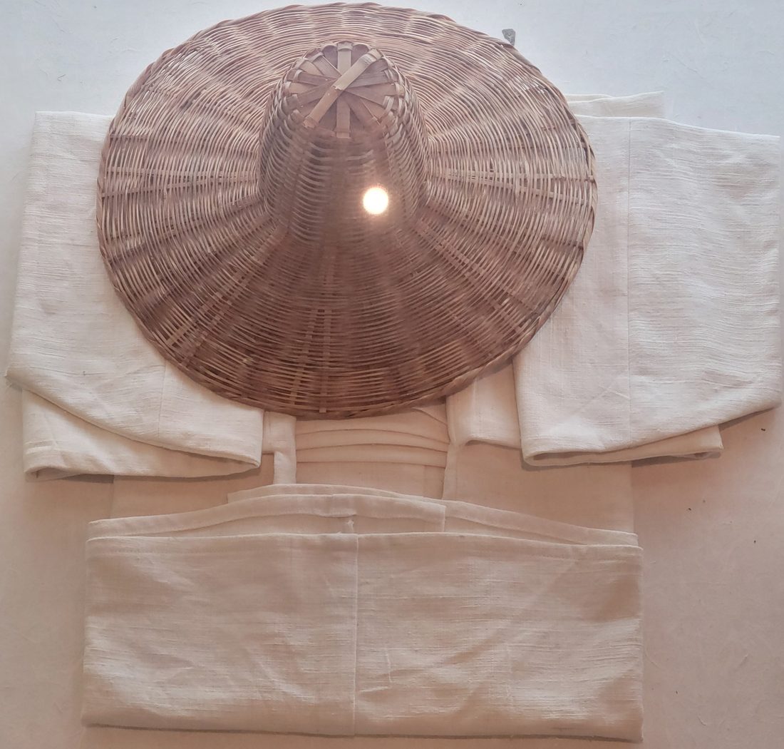 Chapéu cônico de fibra trançada, de aba larga, sobre roupas claras de tecido cru