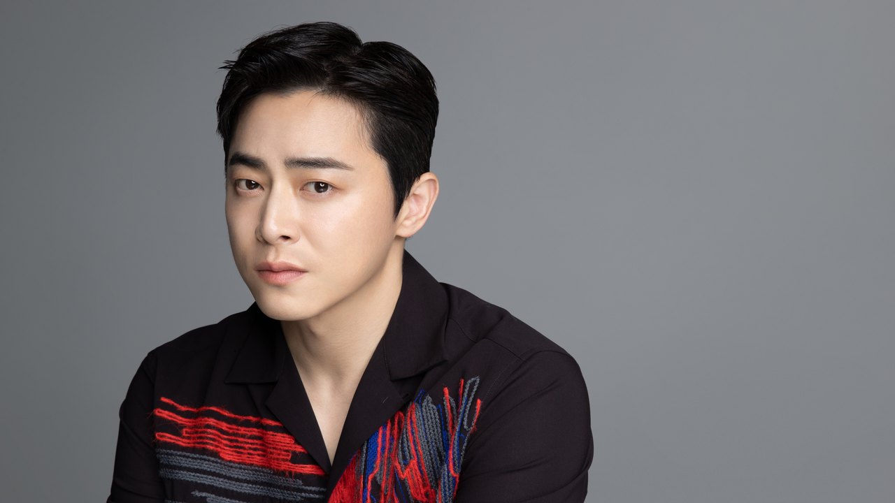 Cho Jung-seok de camisa escura com detalhes vermelhos, em retrato de estúdio com fundo cinza
