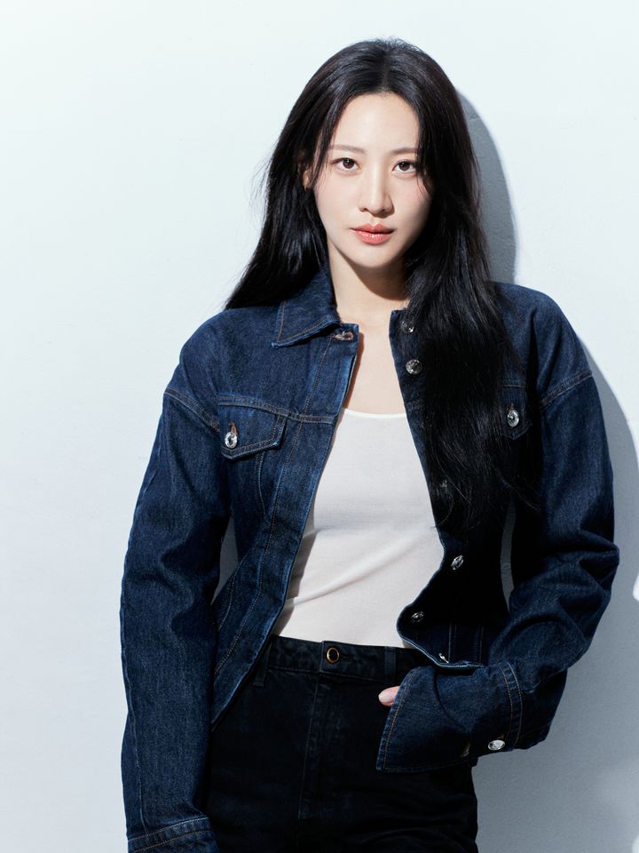 Claudia Kim de jaqueta jeans e blusa branca, em pé num estúdio claro