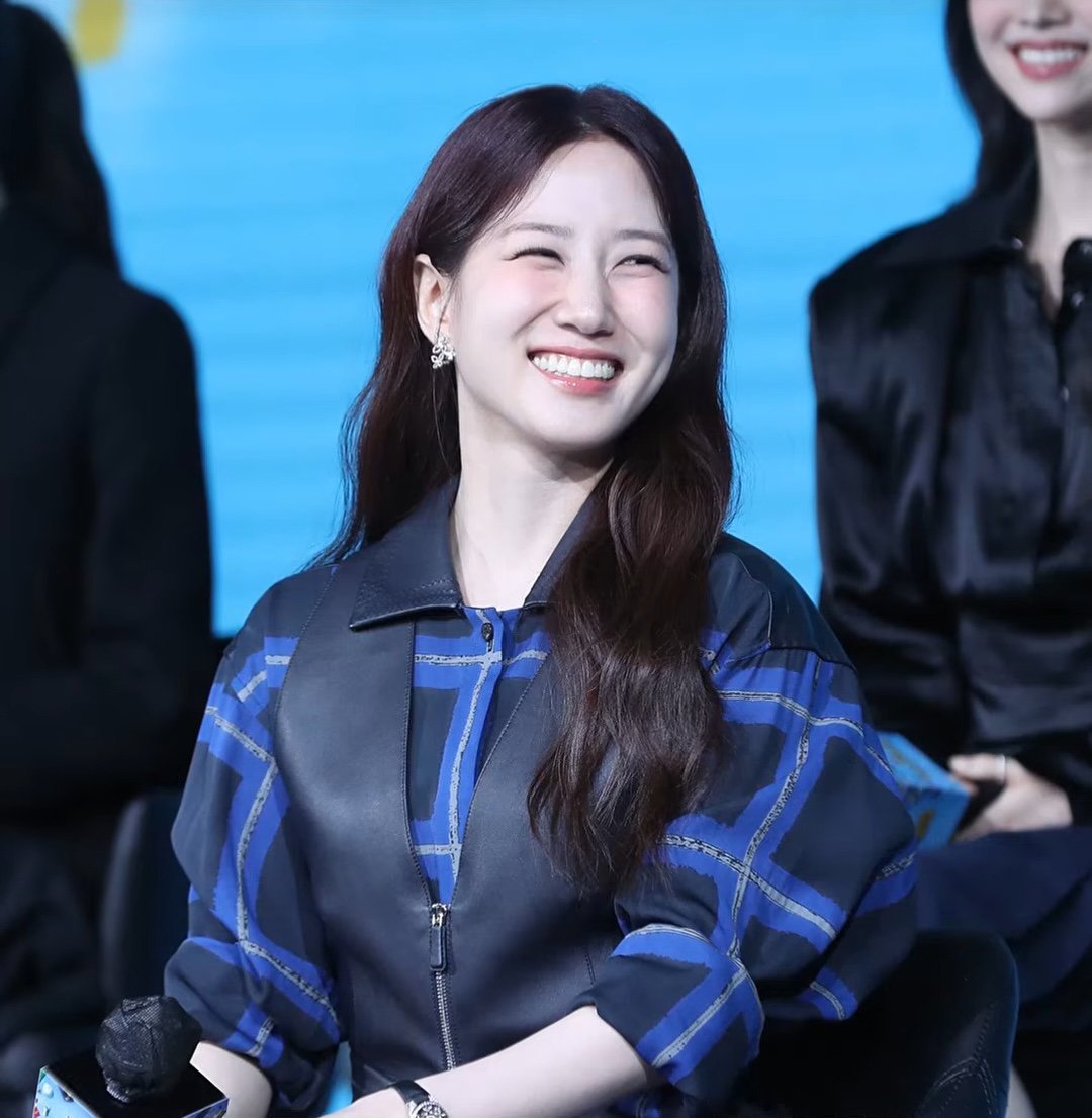 Park Eun-bin de jaqueta xadrez azul ri sentada com microfone na mão diante de fundo azul