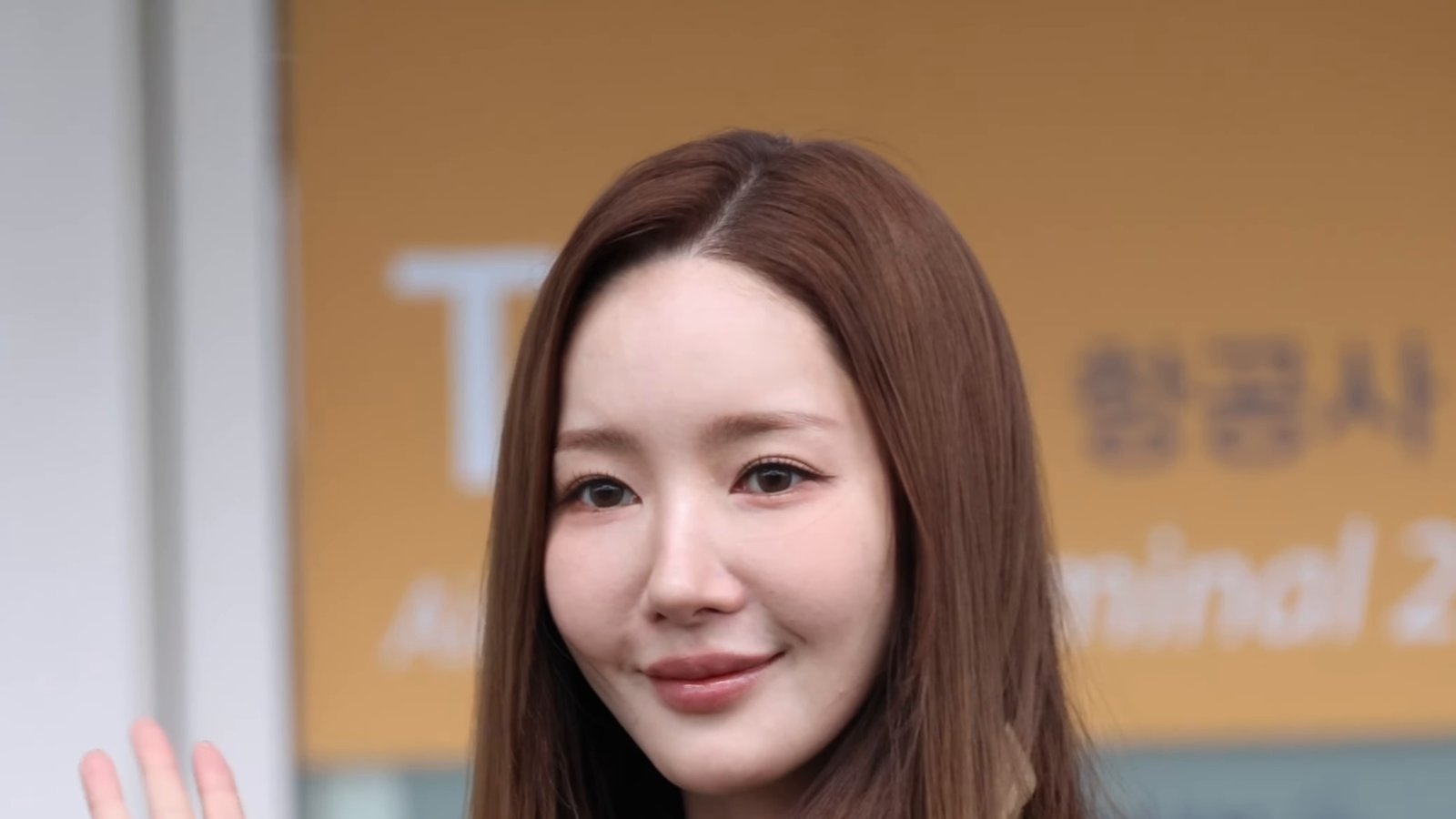 Park Min-young de cabelo longo e casaco bege acena no aeroporto de Incheon
