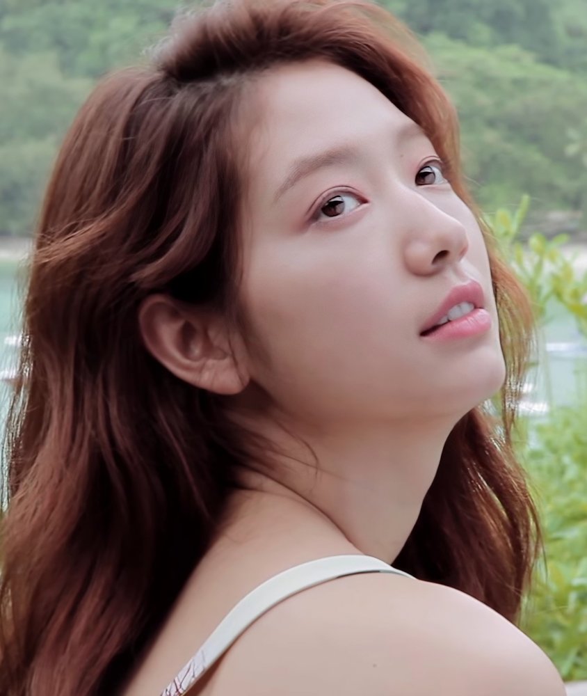 Park Shin-hye de cabelo ruivo ondulado olha para o alto diante de vegetação verde