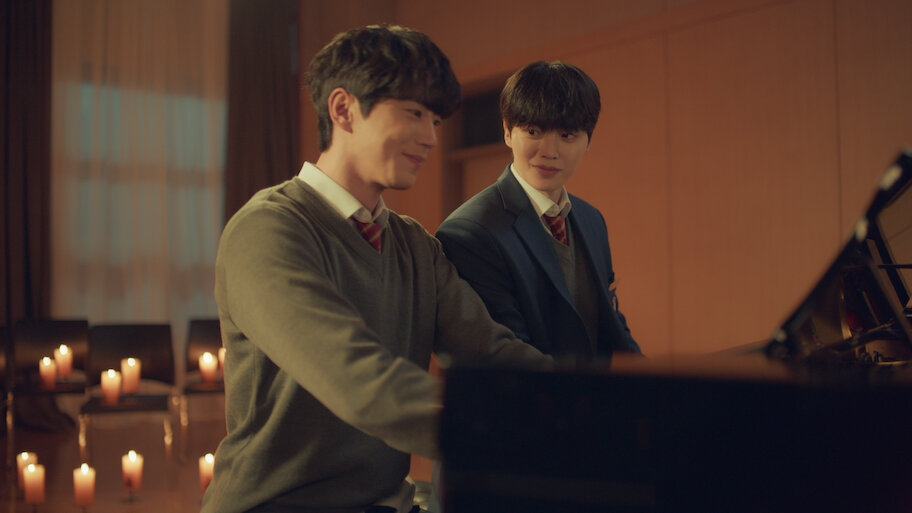 Song Kang e Lee Jun-young sentados ao piano em imagem promocional da Netflix