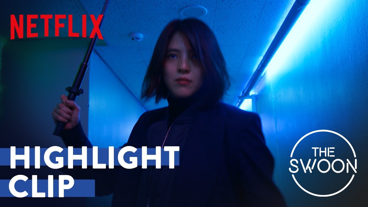 Han So Hee de cabelo curto, com um bastão na mão, em um corredor com luz azul de neon, em cena de My Name
