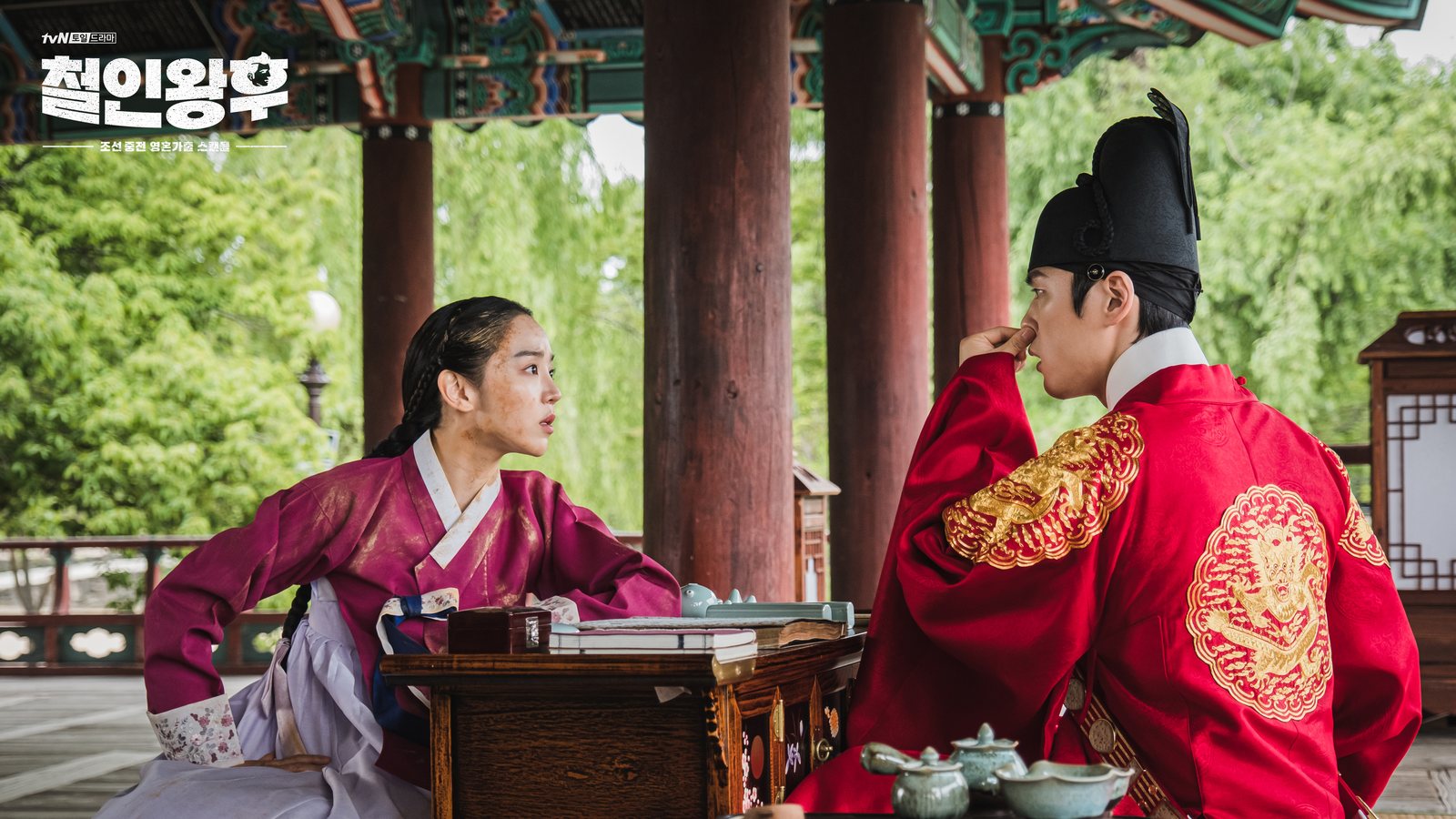 Shin Hye-sun como So-yong, de hanbok magenta e rosto sujo, se inclina sobre uma mesa baixa diante de Kim Jung-hyun como Cheoljong, de manto vermelho real, num pavilhão