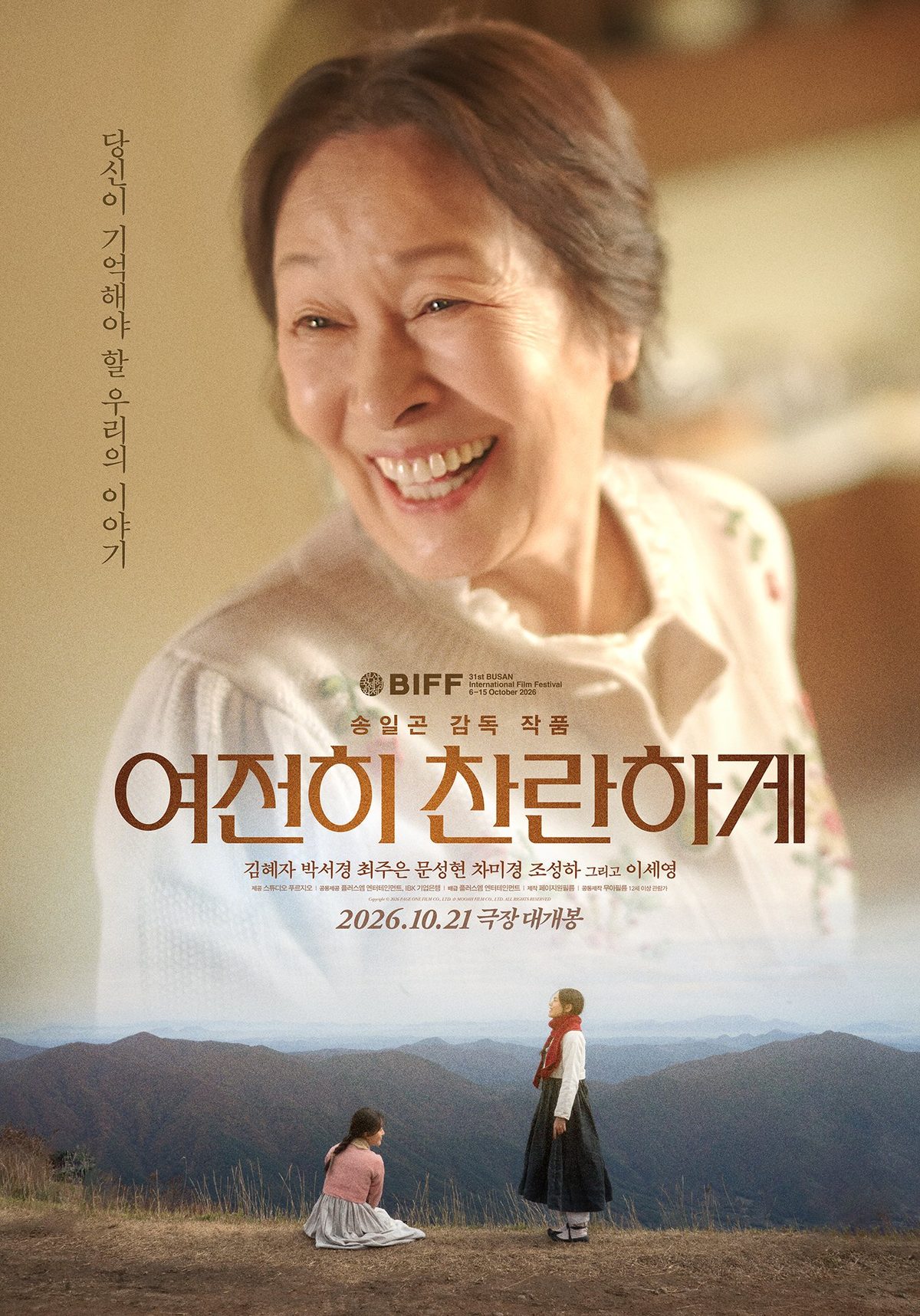 Pôster de Still Shining: Kim Hye Ja sorrindo de blusa branca com flores; abaixo, duas meninas numa colina, uma ajoelhada de rosa e outra em pé de cachecol vermelho; título coreano e data 2026.10.21