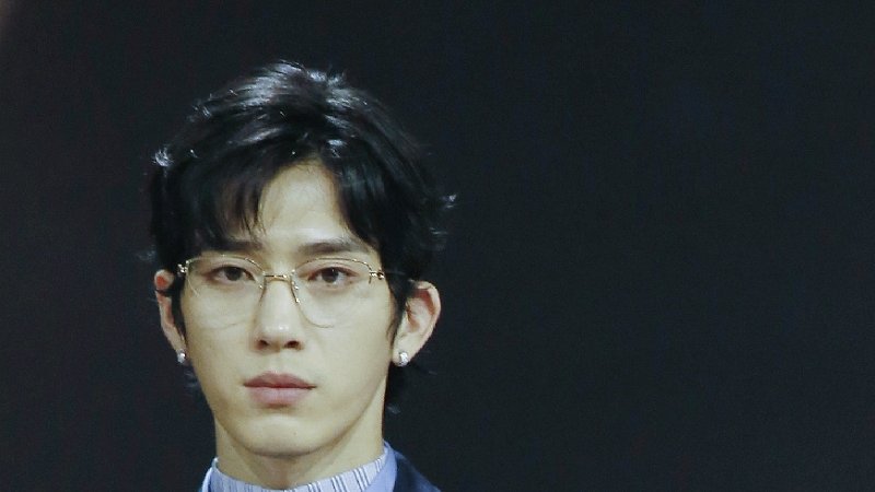 Jing Boran de óculos e camisa listrada azul, de frente, em evento com fundo escuro