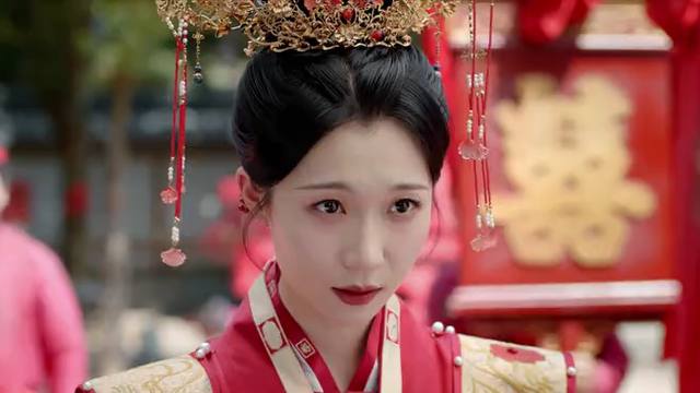 Mulher com coroa dourada de franjas vermelhas e traje de noiva vermelho, diante de um painel vermelho com um ideograma dourado