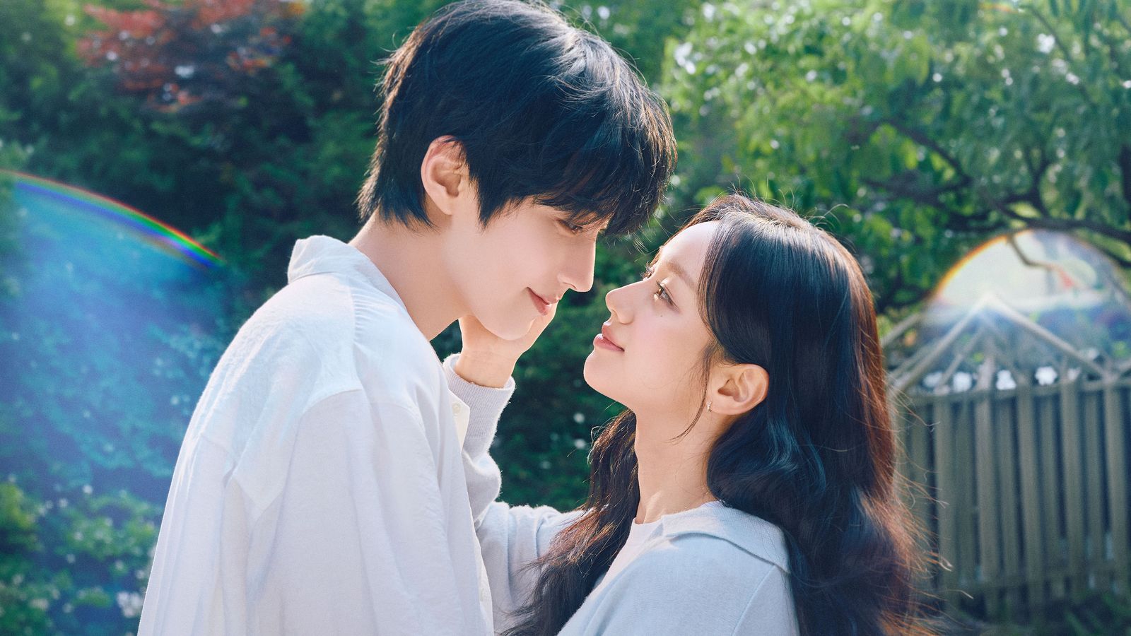 Hwang In-youp e Lee Hye-ri de camisa branca, frente a frente e sorrindo, num jardim com arco-íris ao fundo