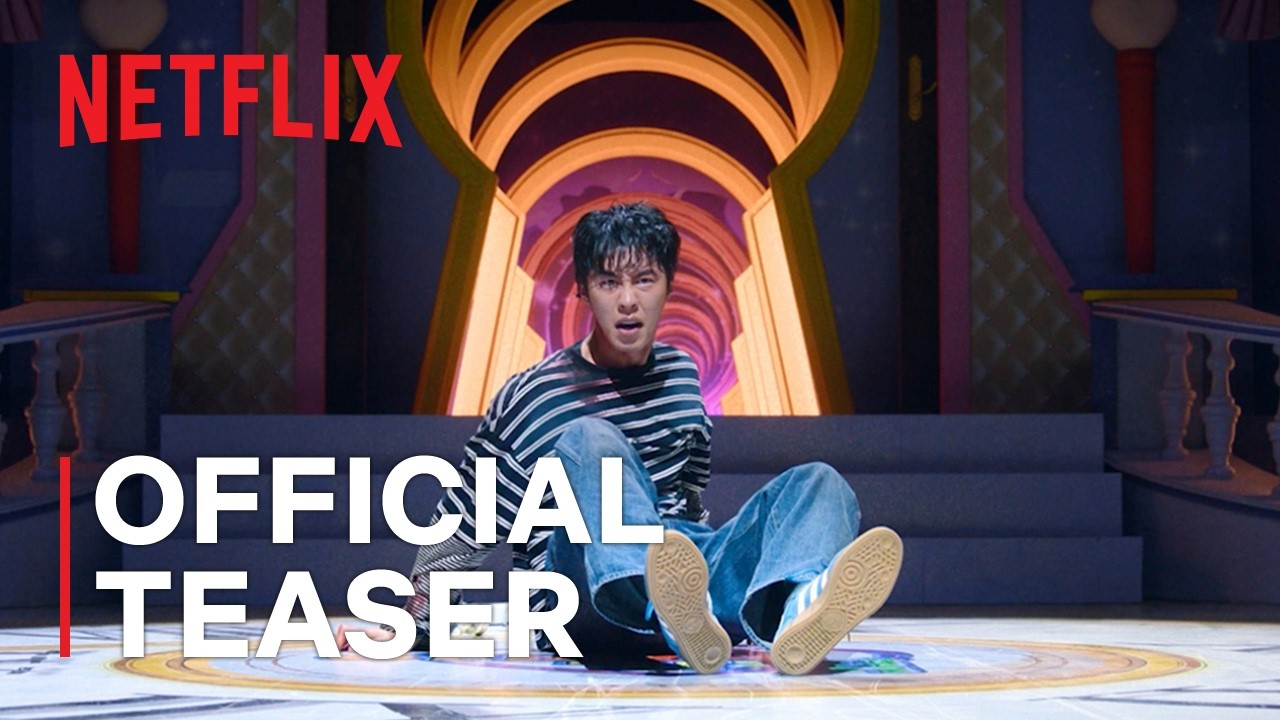Homem de cabelo escuro, camiseta listrada e calça jeans sentado no chão de um cenário colorido com um grande arco em forma de fechadura, em frame do teaser oficial de Dead-End Job, com o logo da Netflix e a legenda Official Teaser